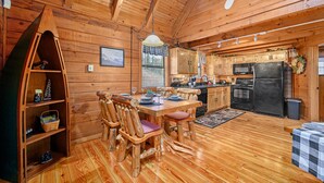 L’intérieur d’un chalet en bois comprend une table à manger, des chaises, un coin cuisine et une bibliothèque en bois.