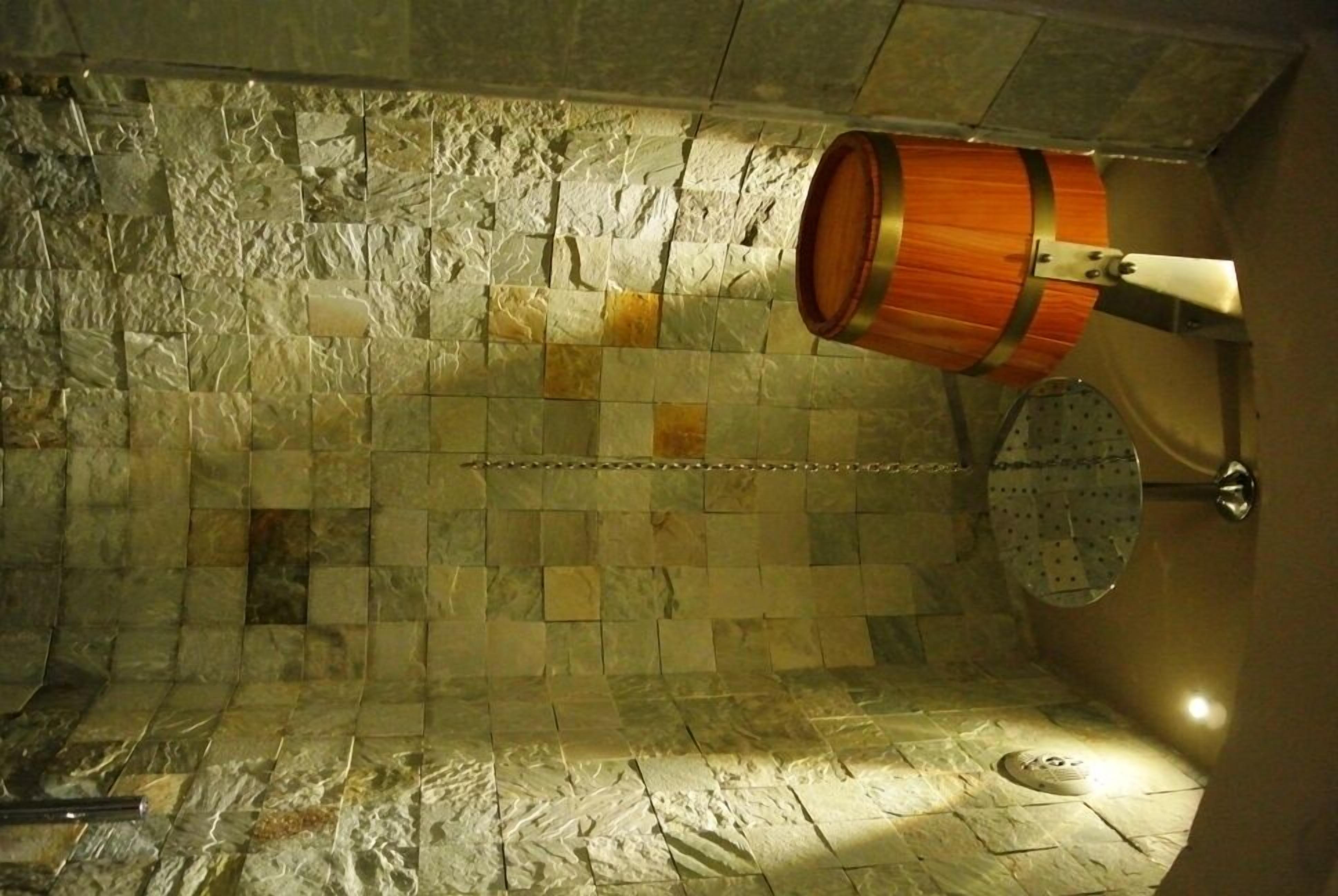 A stone-walled room with a wooden barrel and a metal rack.