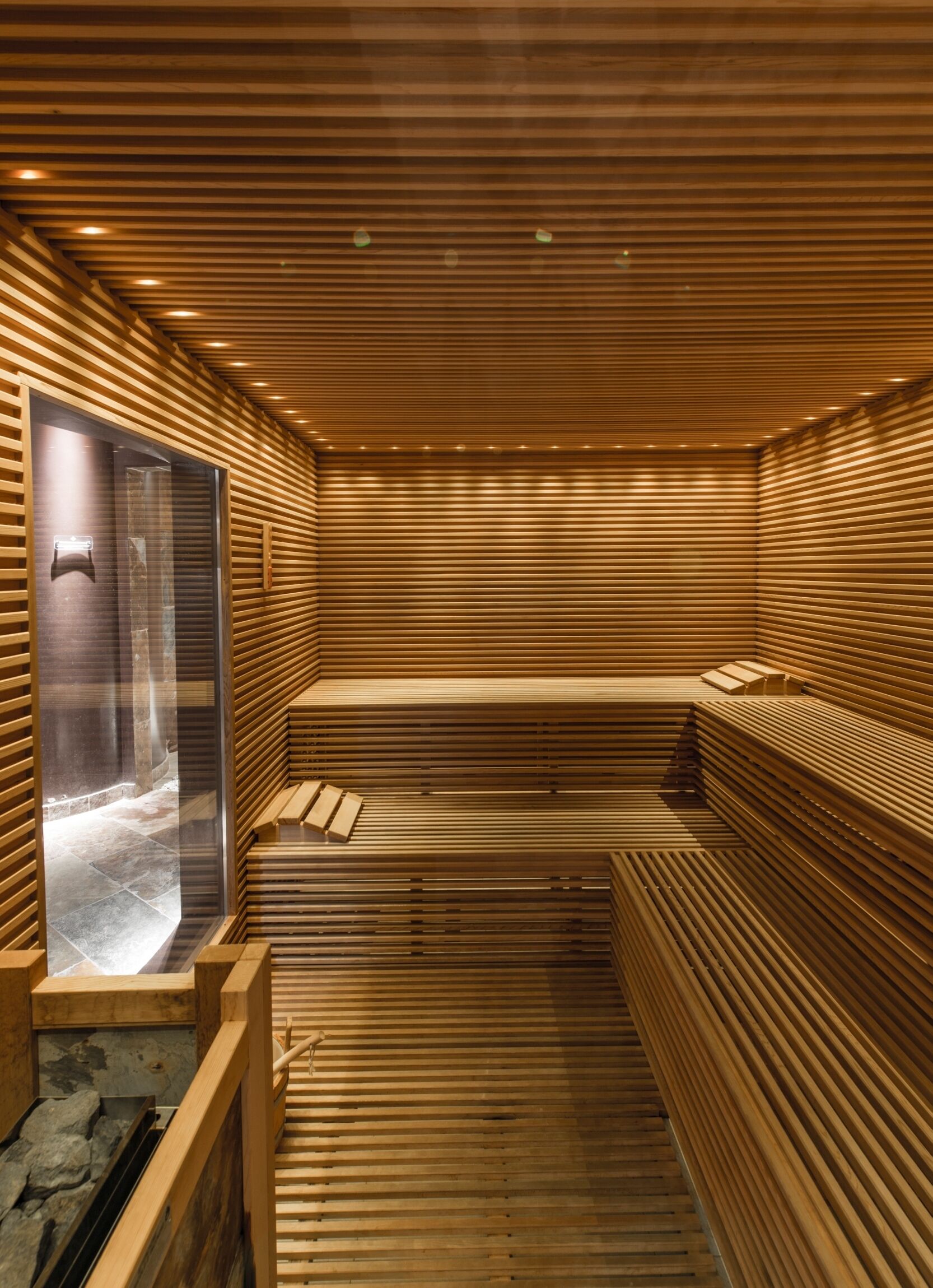 Una sauna con listones de madera, puerta de cristal y un banco.