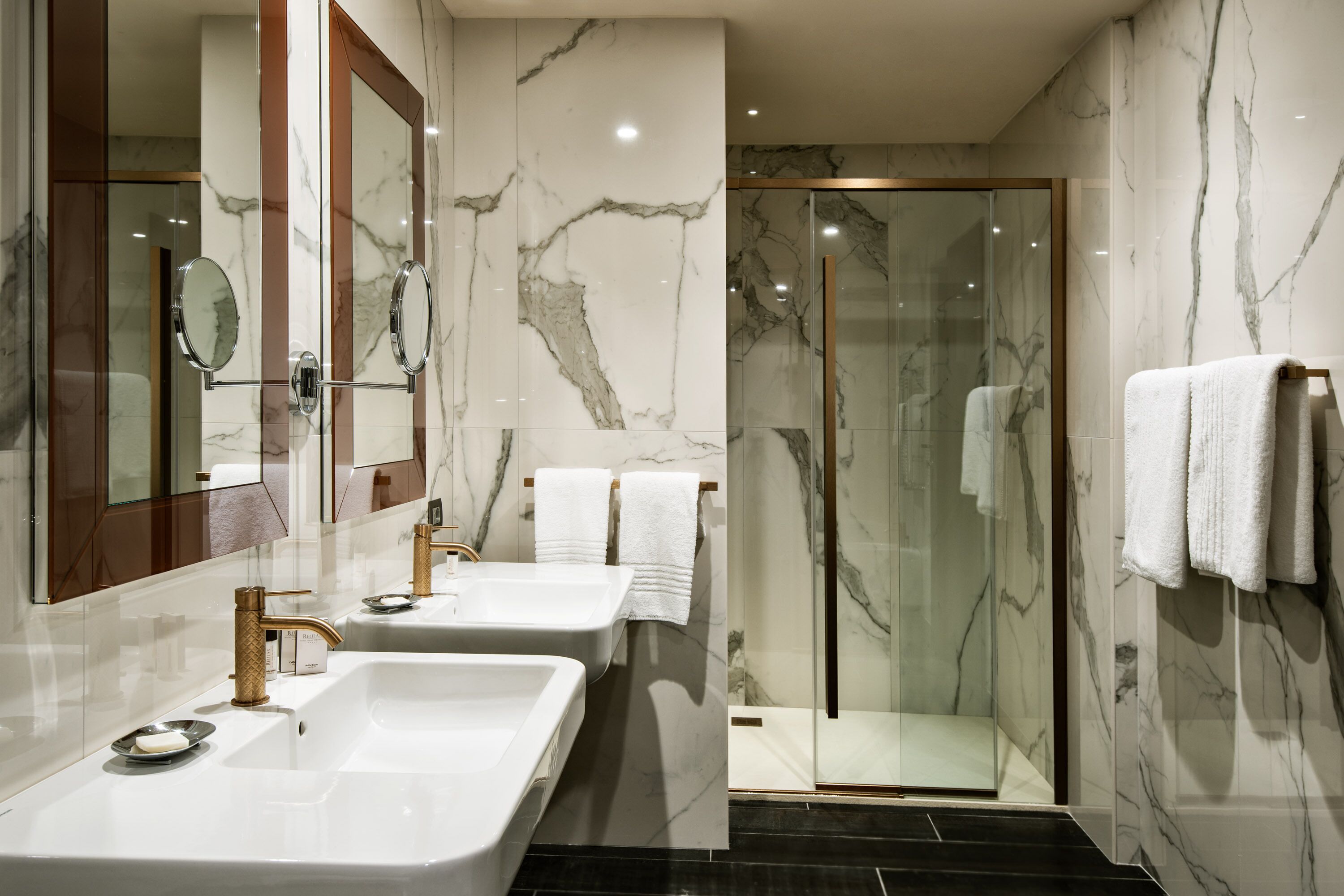 Ein modernes Badezimmer mit zwei Waschbecken, einer Duschkabine aus Glas und Marmorwänden.