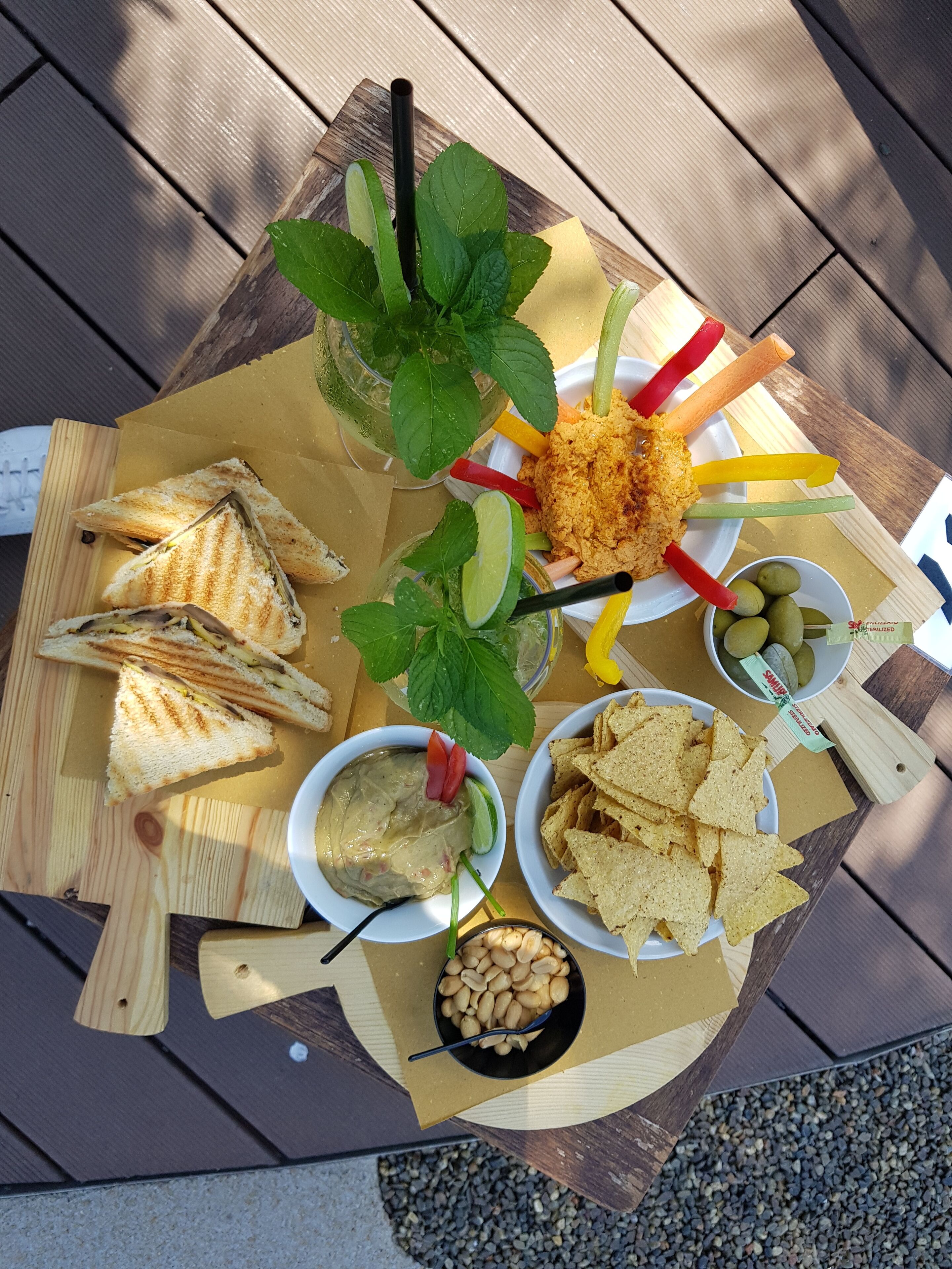 Una mesa de madera con diversos alimentos, como sándwiches, salsas y aperitivos.