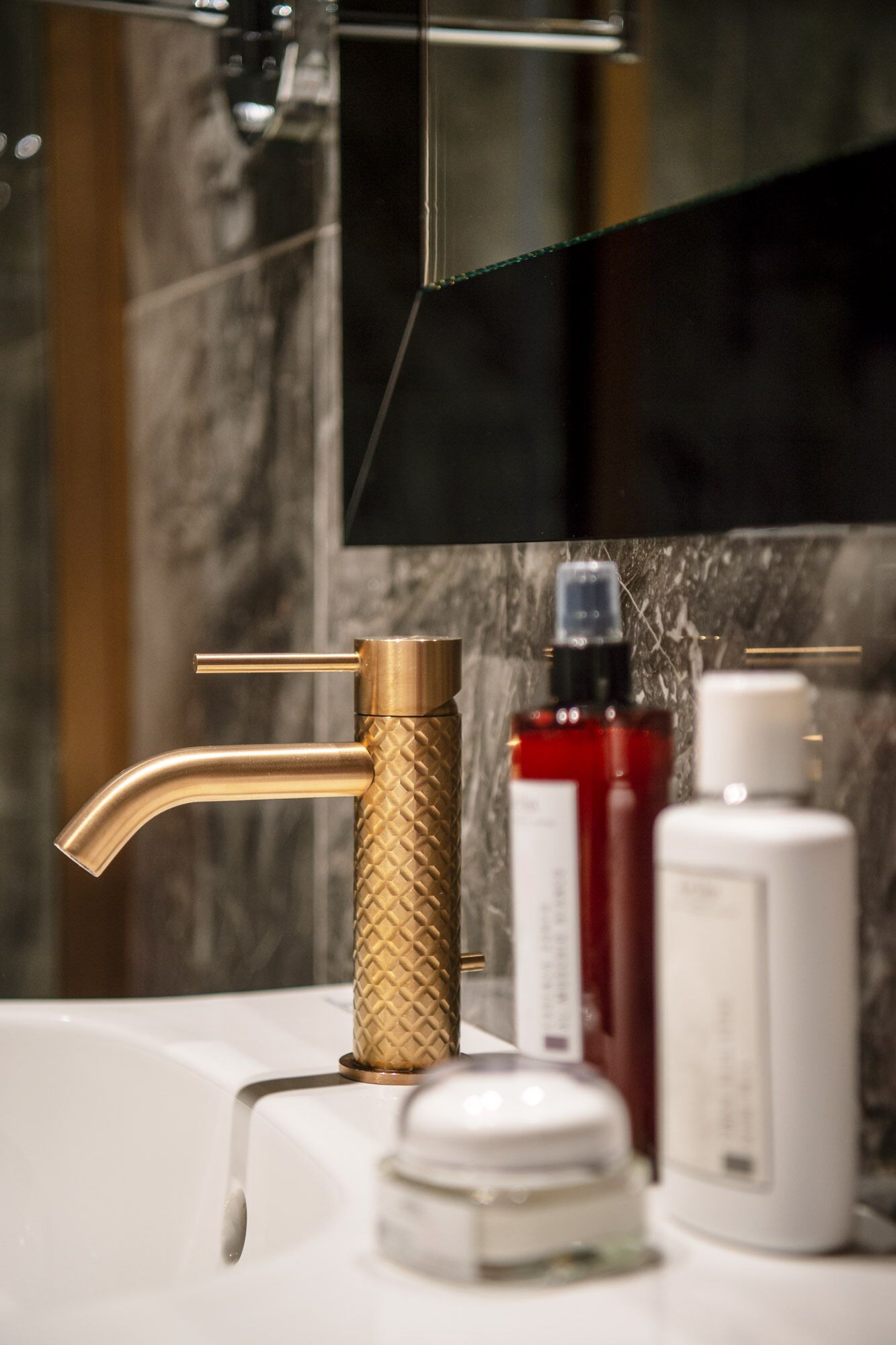 Un baño con grifo dorado, un espejo y dos botellas de artículos de tocador.