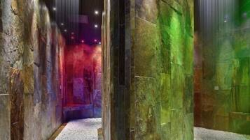 A hallway with a pebbled floor, large stone pillars, and a colorful light display.