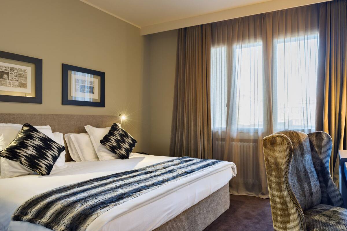Ein Hotelzimmer mit Bett, Sessel, Schreibtisch und Computer sowie einem Fernseher.