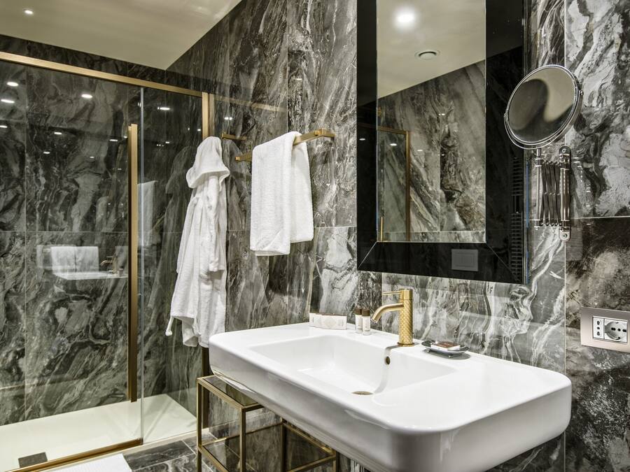 A modern bathroom with a large white sink, gold faucets, and marble walls.
