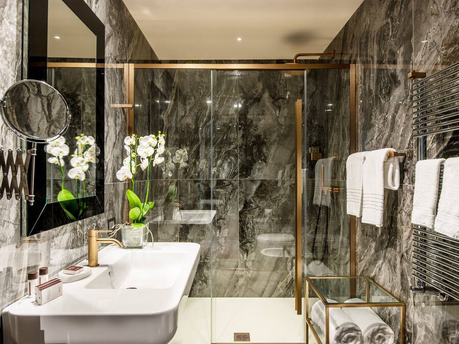 Un baño moderno con pared de mármol, cabina de ducha de vidrio, lavabo blanco y barra para toallas.