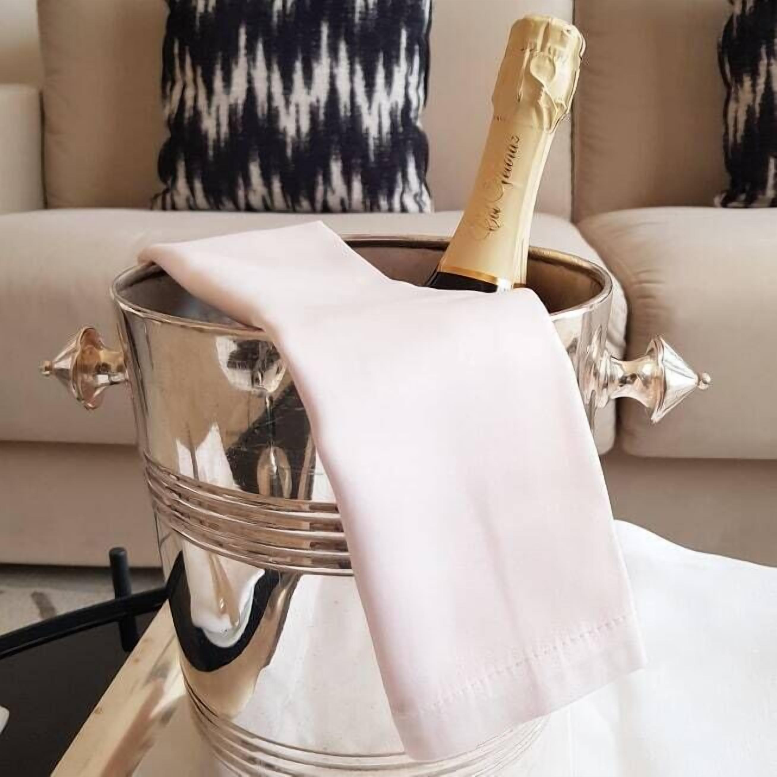 A champagne bottle in a metallic bucket with a white cloth on top, placed on a table in front of a sofa with patterned cushions.
