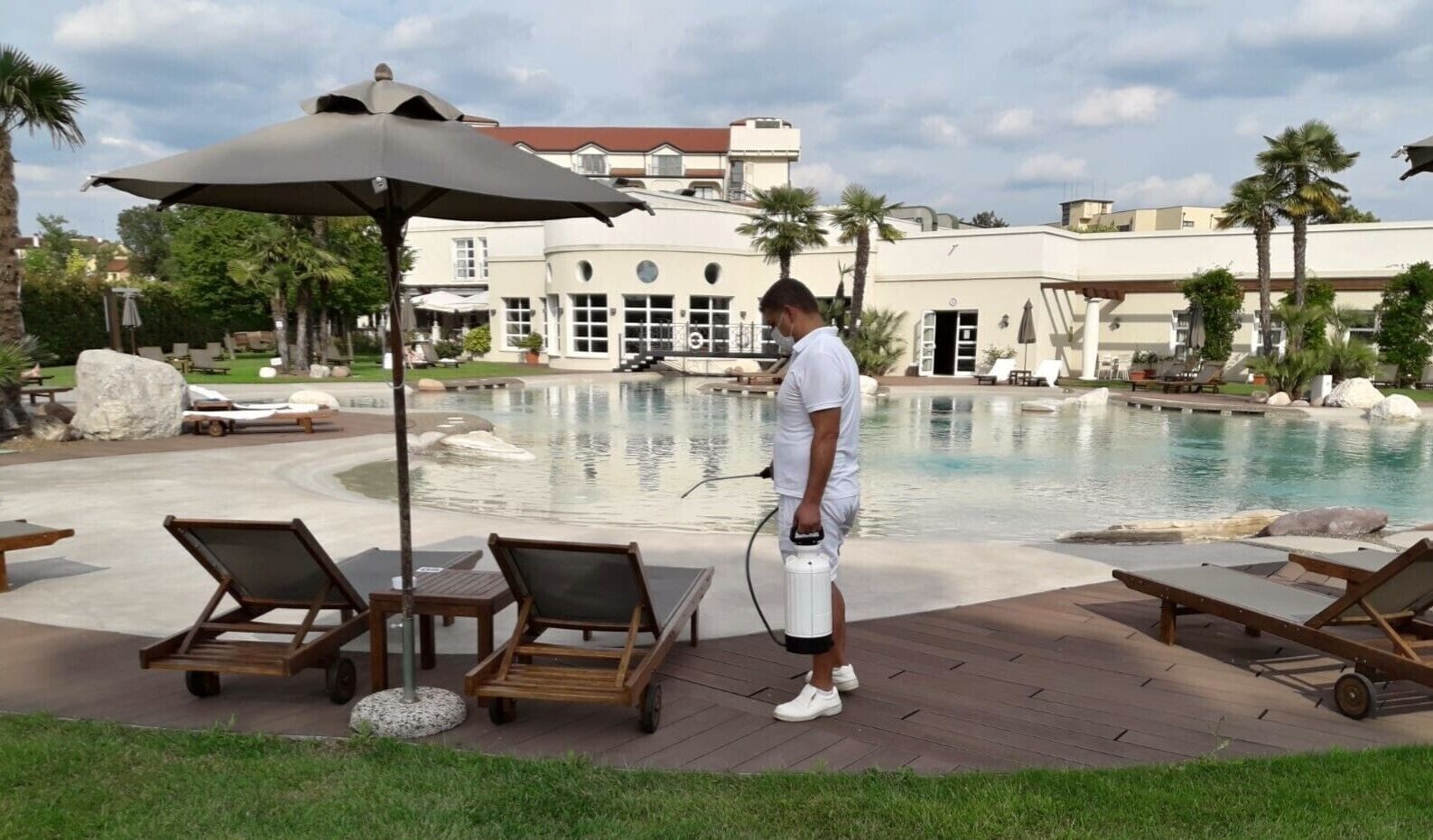 A poolside area with lounge chairs, a large umbrella, and a person using a water sprayer.