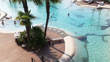 A pool area with lounge chairs, palm trees, and a lifebuoy on the railing.