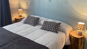 Et soveværelse med en seng, to puder med mønster, et vægtæppe på væggen og to sengeborde med lamper.