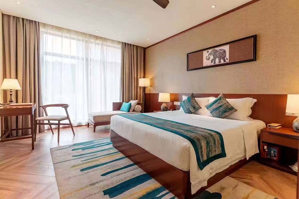 Ein Hotelzimmer mit einem großen Bett, zwei Nachttischen, einem Schreibtisch, einem Stuhl und einem großen Fenster mit Vorhängen.