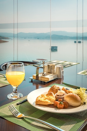 A dining table with a plate of food, a glass of orange juice, and a view of a calm lake and mountains in the background. - Ramada by Wyndham Chenzhou Dongjiang Lake (Chenzhou)