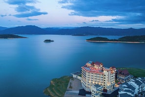A hotel with a prominent sign, surrounded by a large body of water and mountains in the background. - Ramada by Wyndham Chenzhou Dongjiang Lake (Chenzhou)