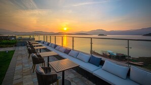 A waterfront patio with outdoor seating and a view of the sunset over the water. - Ramada by Wyndham Chenzhou Dongjiang Lake (Chenzhou)