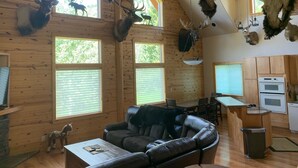 Interno di una baita con pareti in legno, un divano in pelle, zona pranzo e teste di animali montate a soffitto.