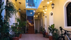 Un estrecho pasillo con baldosas y macetas a ambos lados, que conduce a una escalera.