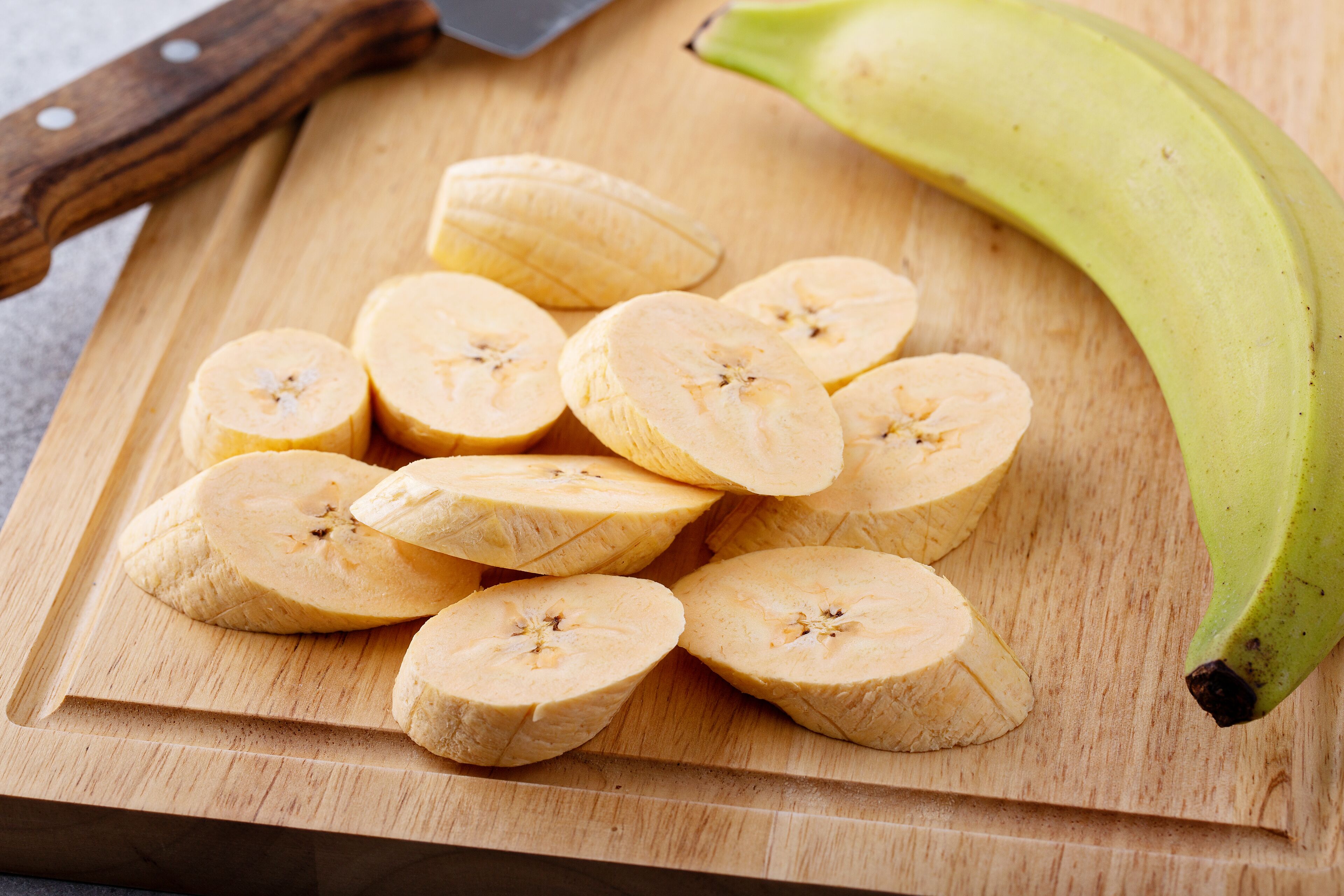 A wooden cutting board with sliced bananas and a whole banana on a kitchen counter.