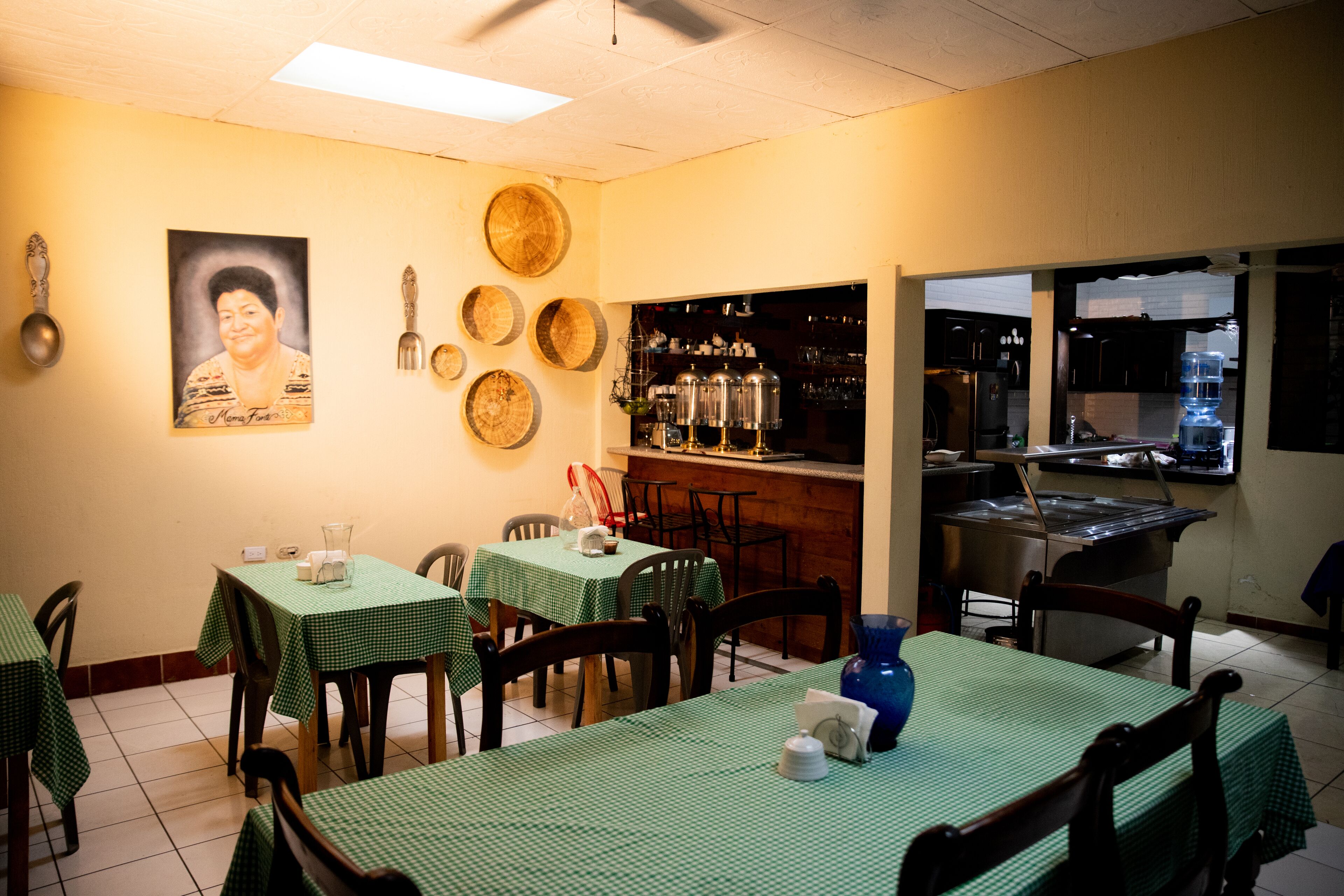 Ein Restaurant mit grünen karierten Tischen und Stühlen, einer Bar mit Regalen voller Flaschen und einem großen Porträt an der Wand.