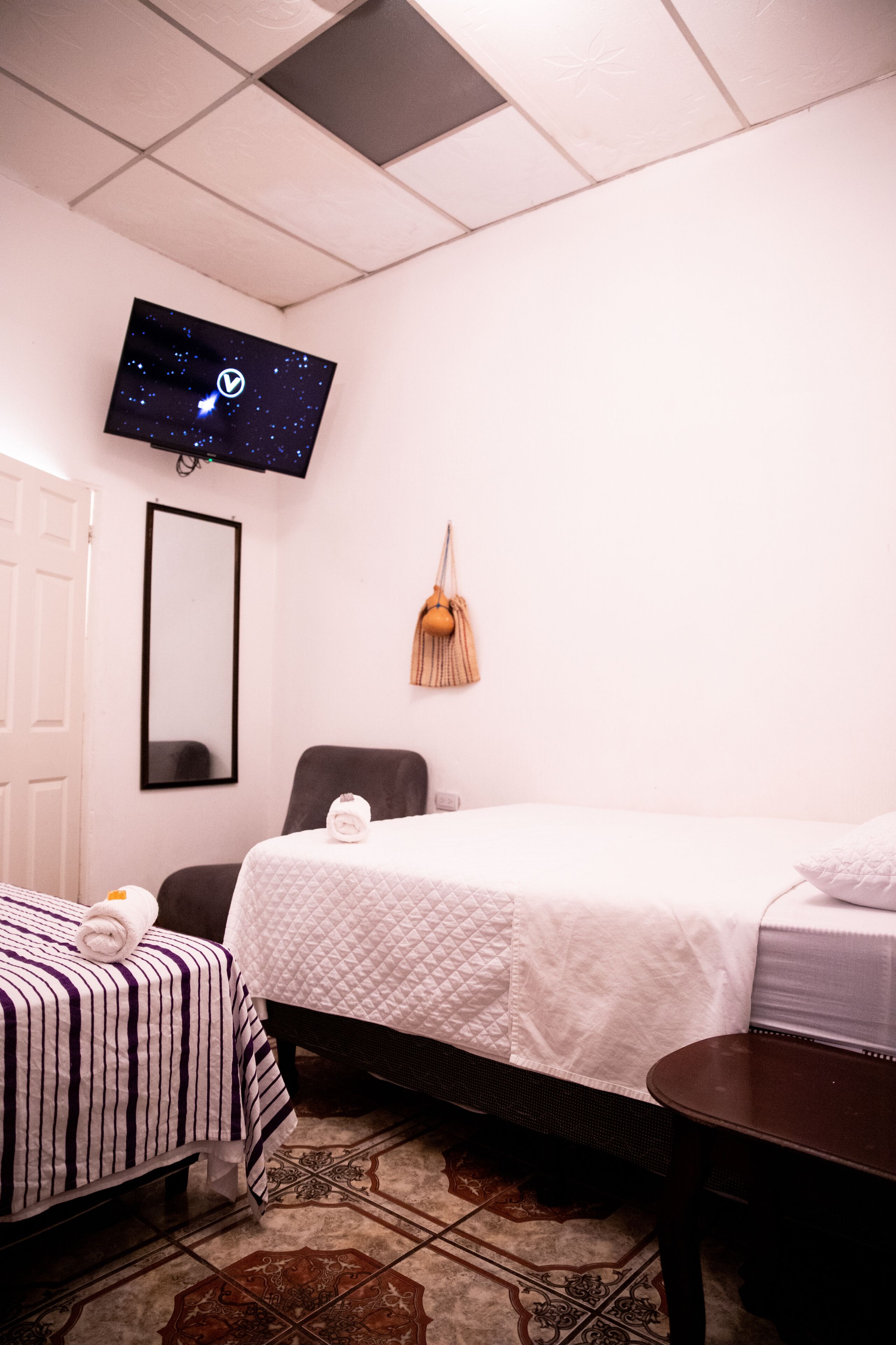 Una habitación de hotel con una cama, una silla, una mesita, un televisor y un espejo.