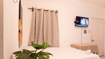 Ein Hotelzimmer mit Bett, Wandfernseher, Vorhang, einem kleinen Tisch und einer Topfpflanze.
