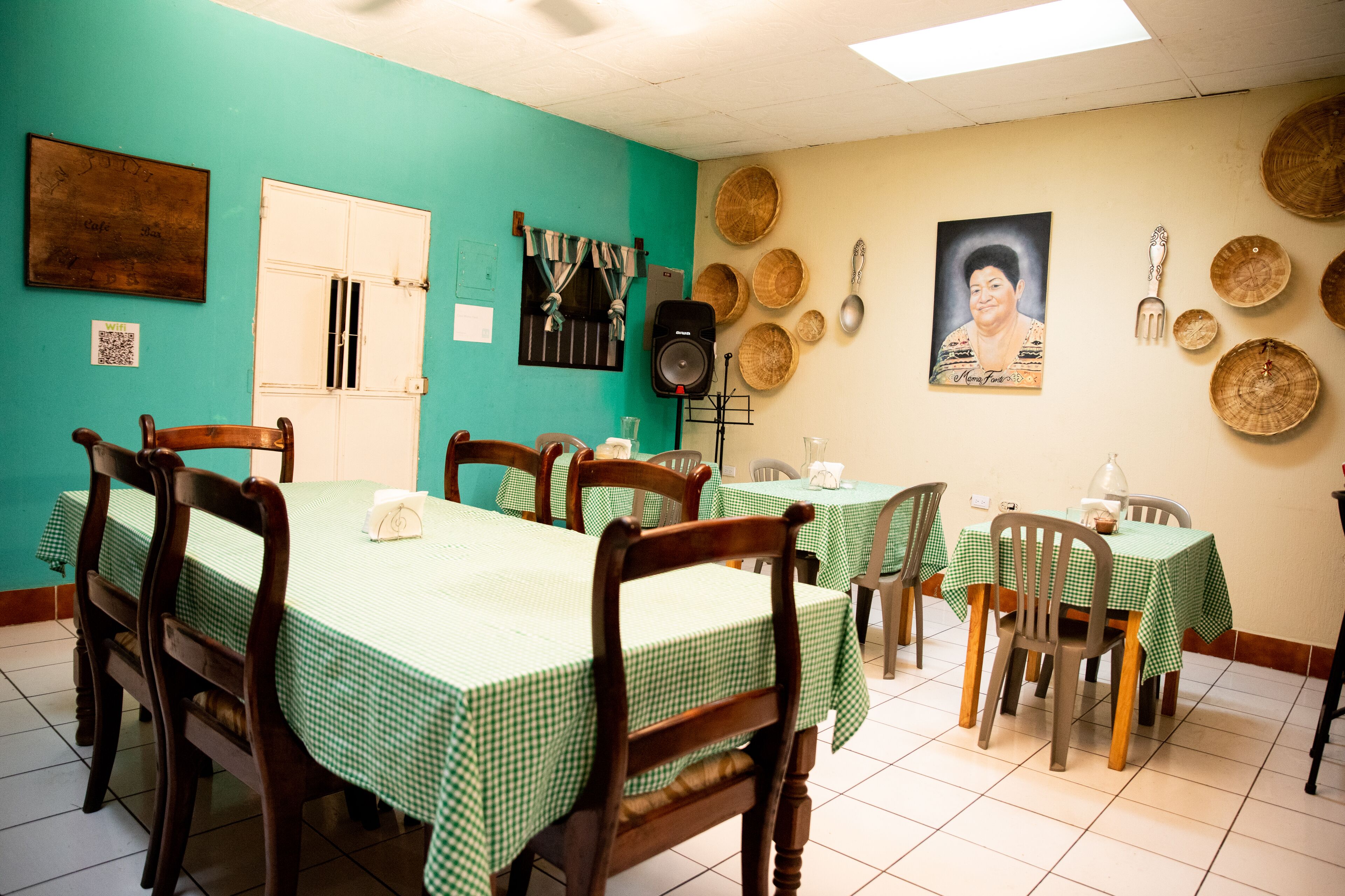 A dining area with green checkered tables and wooden chairs, a speaker, and decorative plates on the walls.