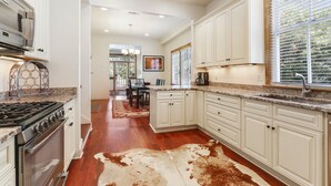A spacious kitchen with white cabinetry, a granite countertop, and a large window with blinds.