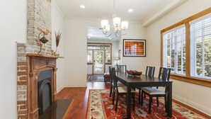 A dining room with a brick fireplace, a chandelier, and a large window with blinds.