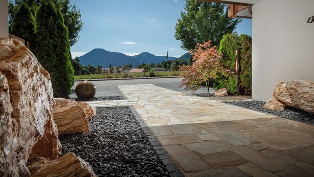 A stone pathway leading to a view of mountains and a church. - Wohnung 3 in Luxury Apartments "R6 Tegernsee" (Bad Wiessee)