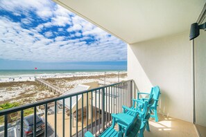 A balcony with a view of the beach, turquoise chairs, and a car parked outside.