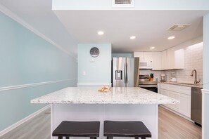 Una cocina con encimera de mármol, electrodomésticos de acero inoxidable y armarios blancos.