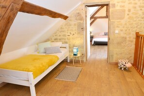 Un dormitorio acogedor en el ático, con techo inclinado, cama blanca con manta amarilla, una mesita de noche pequeña con lámpara, y una decoración con forma de vaca.