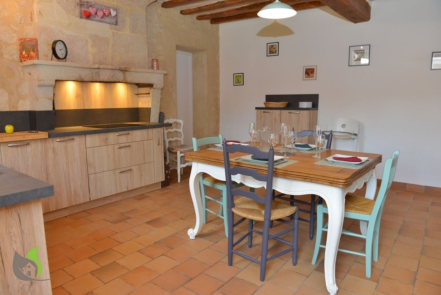 A kitchen with a wooden table set for dining, a stove, and a clock on the wall.
