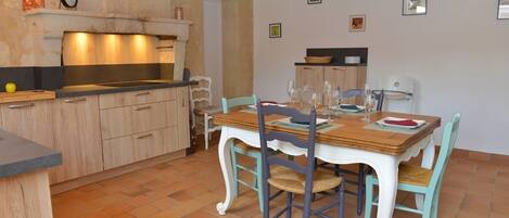 A kitchen with a wooden table set for dining, a stove, and a clock on the wall.