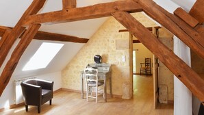 A loft-style room with exposed wooden beams, a stone wall, a desk with a globe, a chair, and a staircase leading to another level.