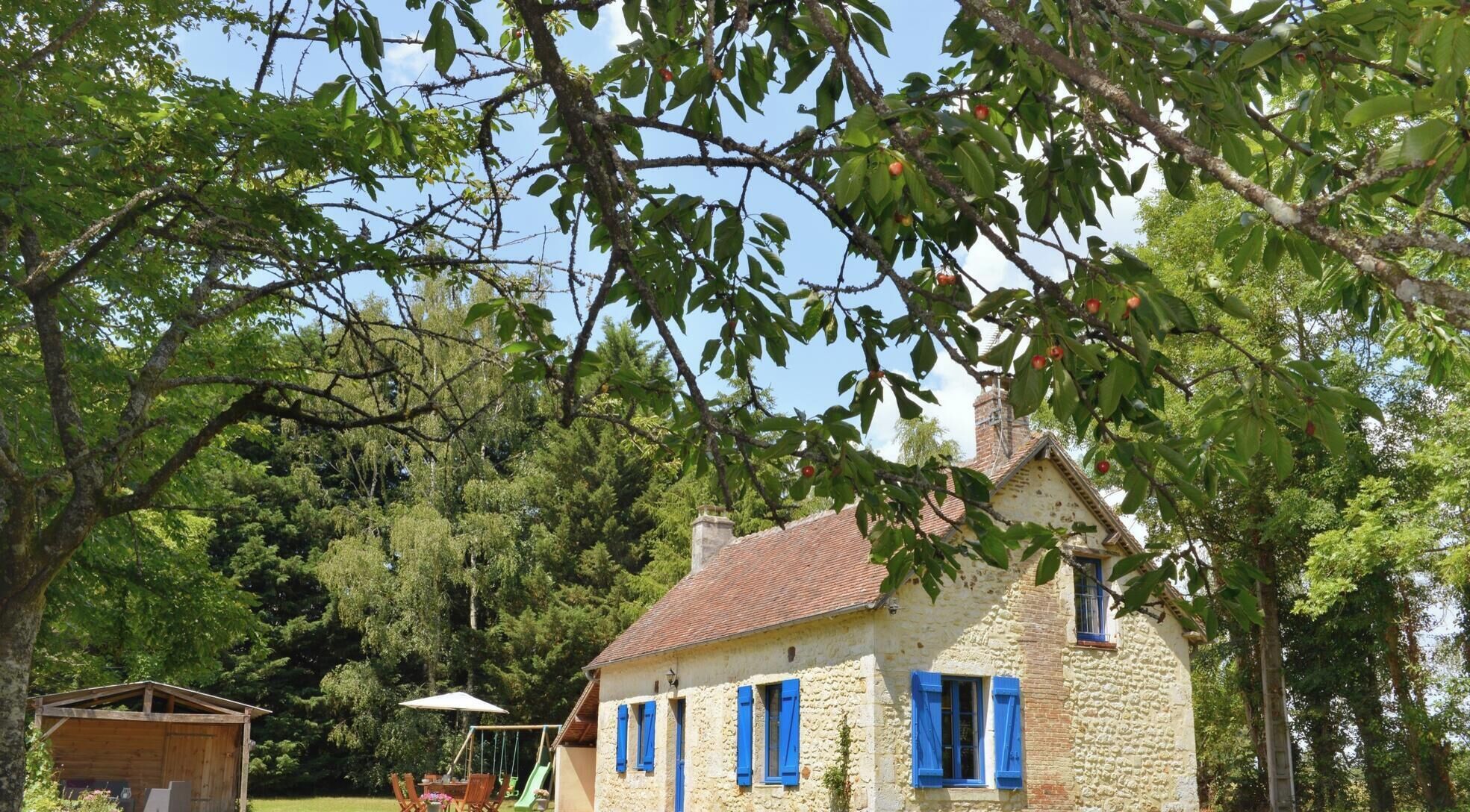 A stone house with blue shutters, a swing set, and a small wooden shelter.