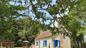 A stone house with blue shutters, a swing set, and a small wooden shelter.