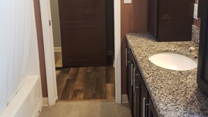 Un bagno con un piano in granito, un lavandino bianco e una porta in legno scuro.