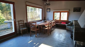 Un comedor con una mesa y sillas de madera, un banco y ventanas amplias con vistas al exterior.