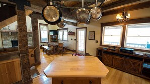 A rustic kitchen with a large wooden island, hanging pots, and a stone fireplace. - Rest and rejuvenate in seclusion at Nature's Nest! (Nashville)
