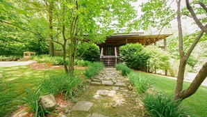 A stone pathway leading to a wooden structure with a porch, surrounded by lush greenery and trees. - Rest and rejuvenate in seclusion at Nature's Nest! (Nashville)