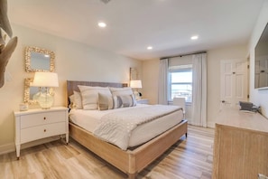 A bedroom with a bed, nightstands, a dresser, a mirror, and a window with curtains.