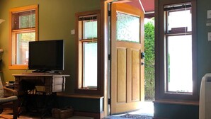 A room with a television on a wooden stand, a door leading outside, and a window with blinds.
