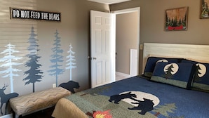 Ein Schlafzimmer mit Bett, Sitzbank, Wand mit Walddrucken und einer Tür.