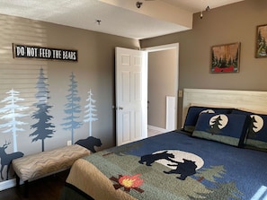 A bedroom with a bed, a bench, a wall with forest-themed decals, and a door.