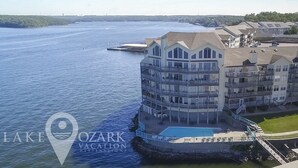 Ein mehrstöckiges Hotel mit Balkonen, die auf ein Gewässer blicken, einem Swimmingpool und einem Steg.