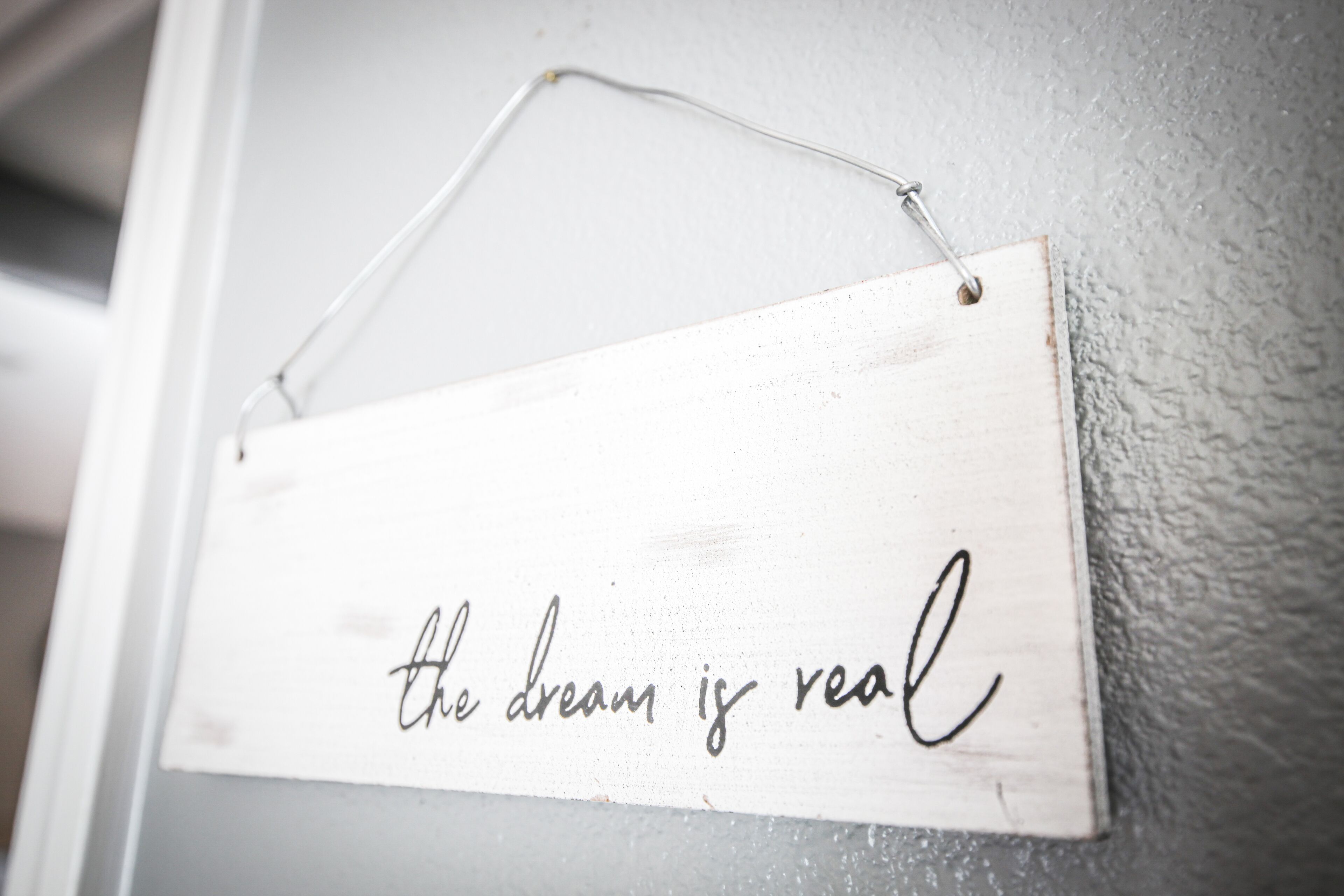 A wooden sign with the phrase "the dream is real" hanging on a textured wall.