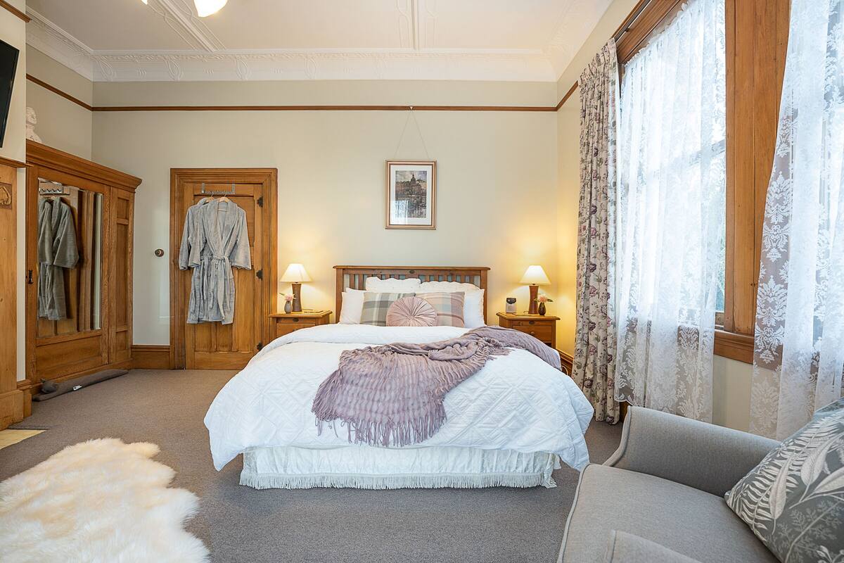 A bedroom with a large bed, wooden wardrobe, and a sitting area with a sofa.