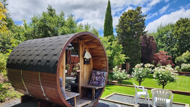 A cylindrical wooden pod with a sloped roof, a small porch, and a seating area with a bench and a chair. - The Fern & Thistle Boutique Accommodation - Drinks, Hotpool, Sauna (Benhar)