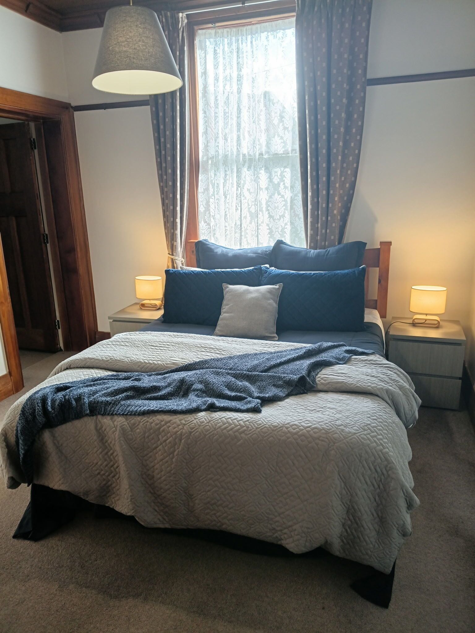 A bedroom with a bed, two bedside lamps, a window with curtains, and a door.