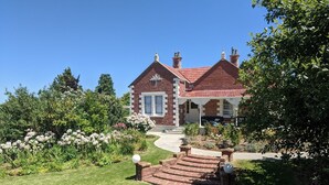 A brick house with a red roof, a front porch, and a well-maintained garden with flowers and a lawn. - The Fern & Thistle Boutique Accommodation - Drinks, Hotpool, Sauna (Benhar)